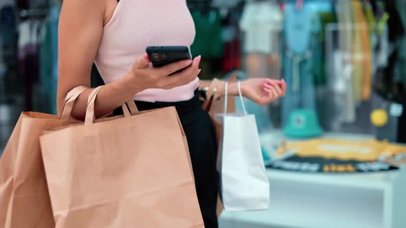 Unrecognizable Pretty Woman Going at Store Mall Showcase with Paper Shopping Bag Smartphone Closeup