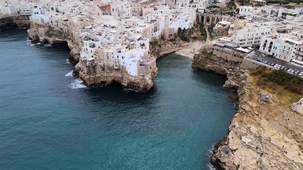 Aerial drone shot, pull back from a small gulf, rocky beach, revealing Polignano A Mare, Italy.