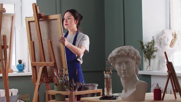 Pretty Woman Artist Puts a Canvas on Easel and Starts Drawing