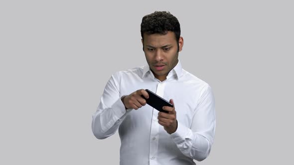 Infantile Young Darkskinned Man Playing Video Game on His Smartphone