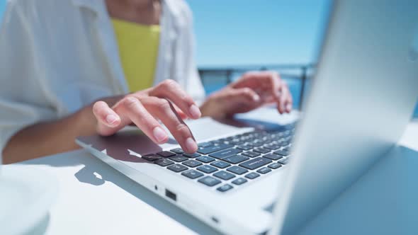 Woman Typing on Laptop Keyboard Outdoors on Terrace with Beautiful Sea View