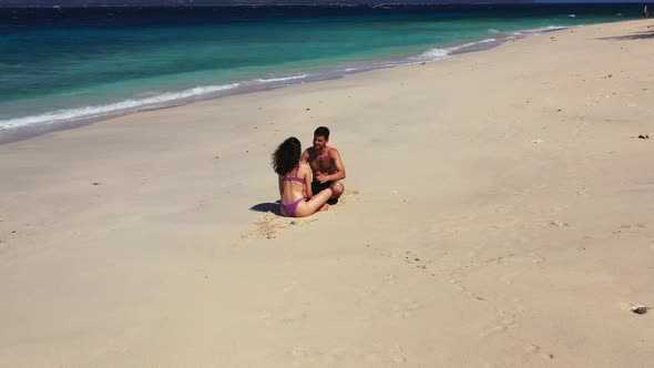 A young happy couple sitting on the warm sand of an Australian beach, bathing in the sunlight