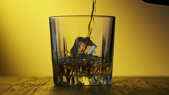 Whiskey Poured in Glass at Yellow Background. Glass of Whisky with Ice Cubes