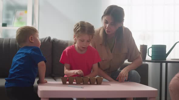 Girl Puts Seeds Into Seedling Tray with Mother and Brother