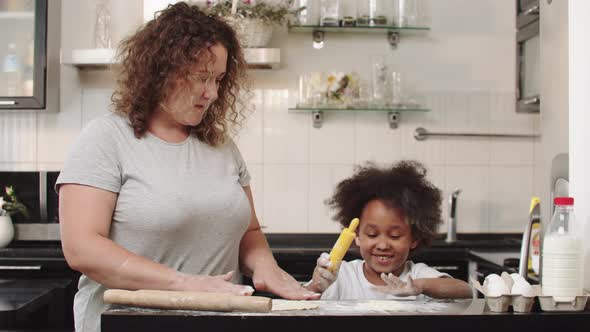 Black Little Girl with Her Mother Making Dough in the Kitchen