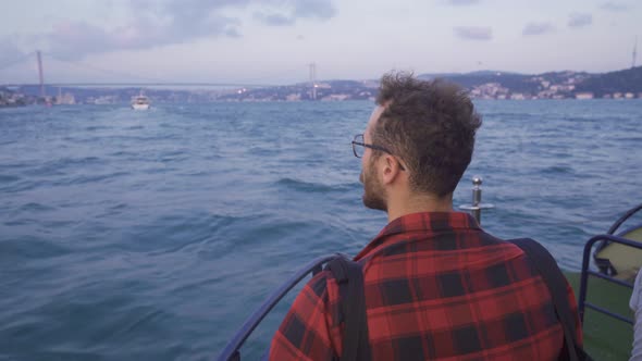 Young man watching the Bosphorus bridge and the city from the ferry.