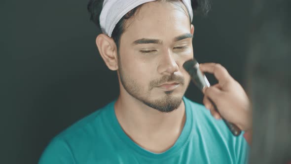 Close up of professional make up artist contours a man's face and doing the make up