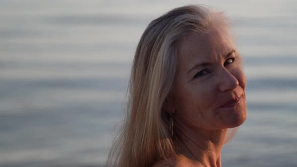 Beautiful mature blonde woman looks into the setting sun and then turns to look at the camera in a p