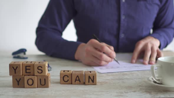 Motivating Message Yes You Can Solved Using Cubes. Man Works At Table, Checking Documents