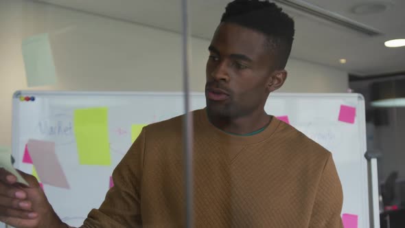 African american businessman standing behind glass wall in meeting room using sticky notes