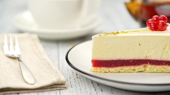 Redcurrant Cheesecake on a Plate on White Wooden Background. Blurred White Cup of Tea and Teapot in