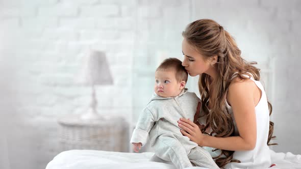 Caring Beautiful Mother Kissing and Caress Newborn Cute Baby Showing Love and Tenderness