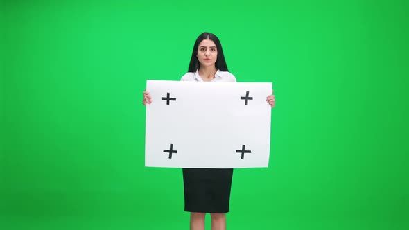 Young Businesswoman in a Suit Standing and Holds a White Paper Poster Template Serious Look at the