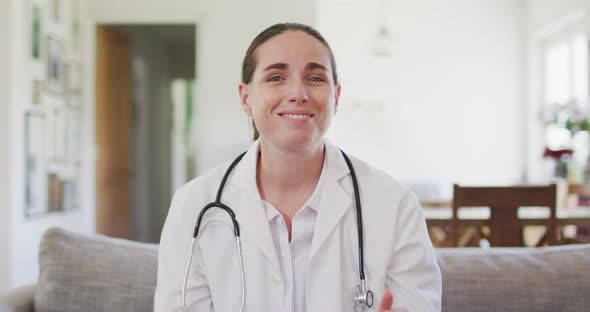 Happy caucasian female doctor sitting on sofa having video call