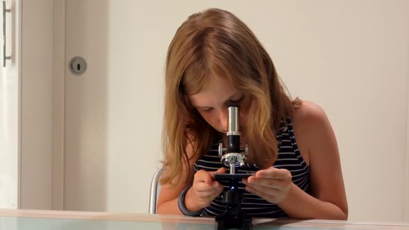 Cute Blond Teenage Girl in Striped Shirt is Looking Through the Microscope Lens