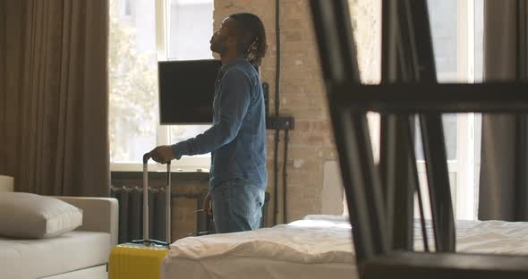 Joyful Relaxed African American Man with Luggage Looking Around in Hotel Room and Falling Back on