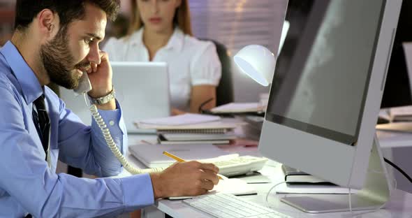 Businessman talking on the phone while writing in diary