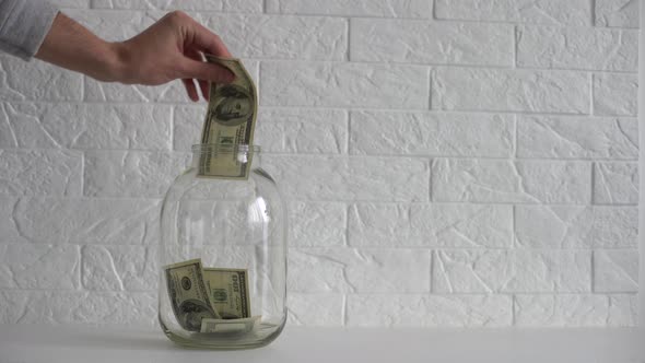 Hand Putting a Dollar Bill in a Savings Jar with a White Label