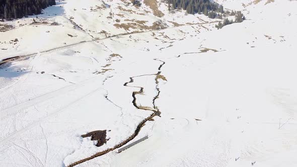 Drone shot ing forwards) of a Stream in the middle of a Snowy Mountain Plain with a Road Behind