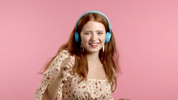 Pretty Young Girl with Red Hair Having Fun, Smiling, Dancing with Blue Headphones in Studio Against