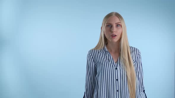 Blonde Young Woman Spreading Her Hands to the Sides and Saying "What" on Blue Background