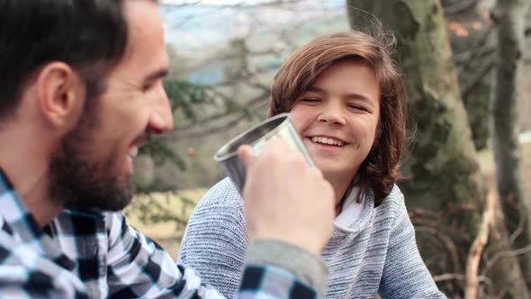 Cheerful man and teenage boy drinking tea during spring hiking