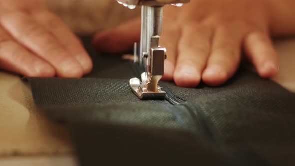 Hand of the seamstress is using white industrial sewing machine sew zipper