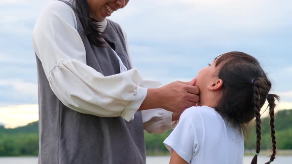 Loving mother touching the face of a smiling little girl and hugging by the lake.