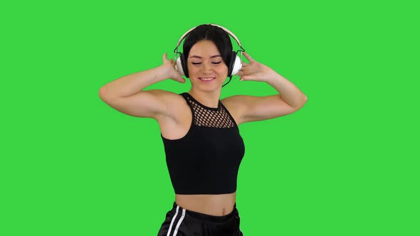 Young Happy Sportive Woman Listening Music in Headphones and Dancing on a Green Screen, Chroma Key.