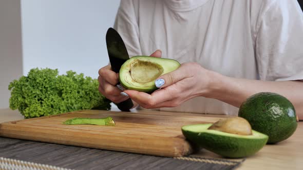 Female Hands Clean the Crust Avocado