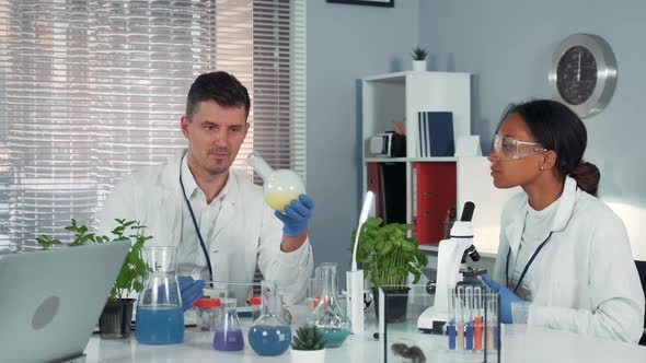 Research Scientist Providing Experiment with Liquid in Flask While His Collegue Observing the