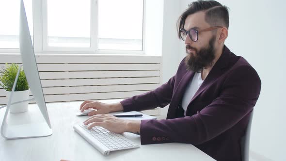 Concept of Office Work or Freelancing. Young Bearded Stylish Man Working at the Computer in the