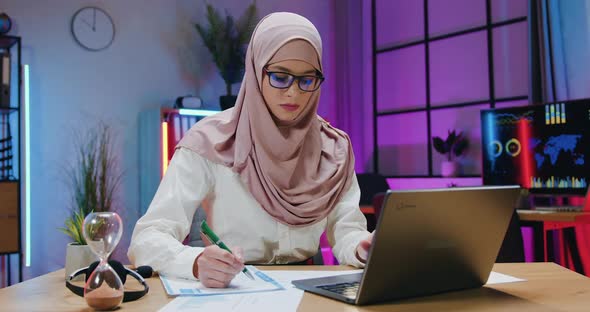 Arabian Businesswoman in Hijab Checking Information on Laptop Screen with Datas on Financial reports