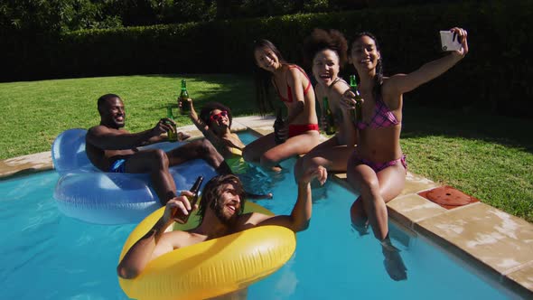 Diverse group of friends sitting at the poolside drinking beer and taking a selfie