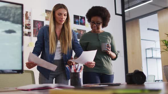 Two diverse female colleagues discussing and looking at images standing in office