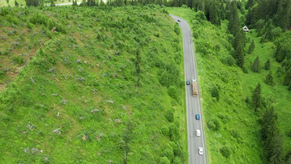 Aerial View of the Road with Driving Cars and Truck in the Mountains with High Green Fir Foliar Pine
