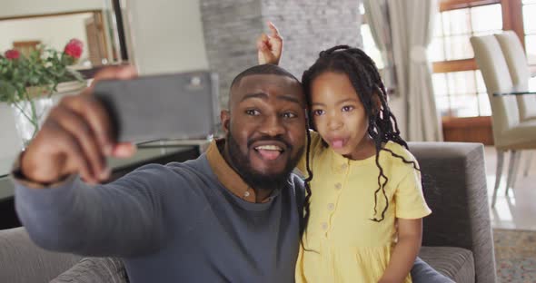 Happy african american daughter and father taking selfie on sofa