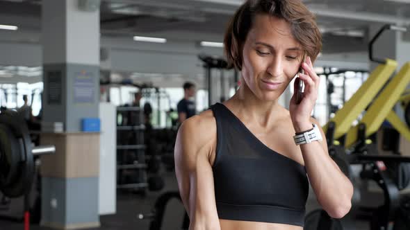 Mature Woman is Making Biceps Exercise with Dumbbells in Gym and Speaking Phone