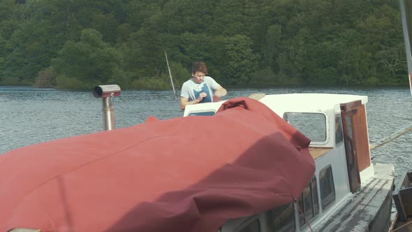 Young man working on boat restoration wipes dust off roof using brush