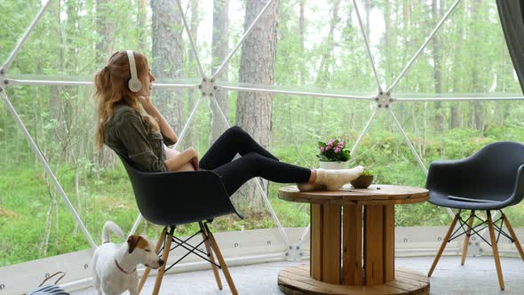 pregnant woman listening to music with headphones sitting by a large window