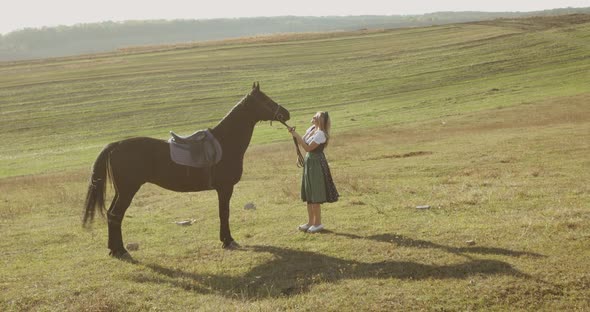 Woman in a Dress Has a Fun and Caresses a Brown Horse Among the Wide Steppes