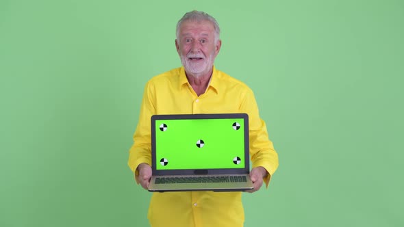 Happy Senior Bearded Businessman Showing Laptop and Looking Surprised