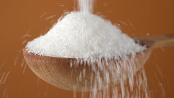 Pouring white sugar in wooden spoon, close up