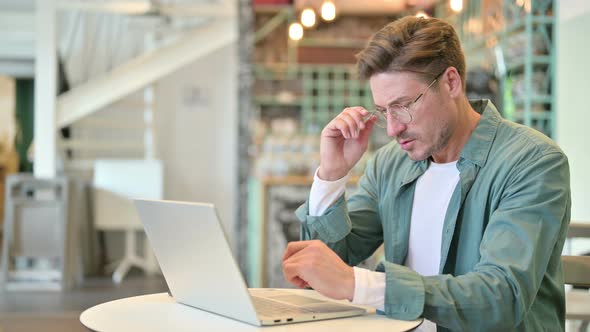 Stressed Middle Aged Man with Laptop Having Headache in Cafe 