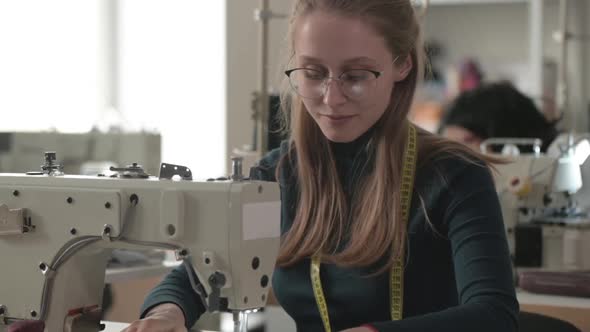 tailor woman sits at workplace with an electric sewing machine and smiles