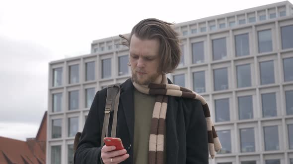 stylish guy in scarf and coat hold mobile phone in a hand at street of Wroclaw, Poland