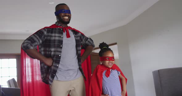 Happy african american father and daughter having fun, wearing superhero costumes