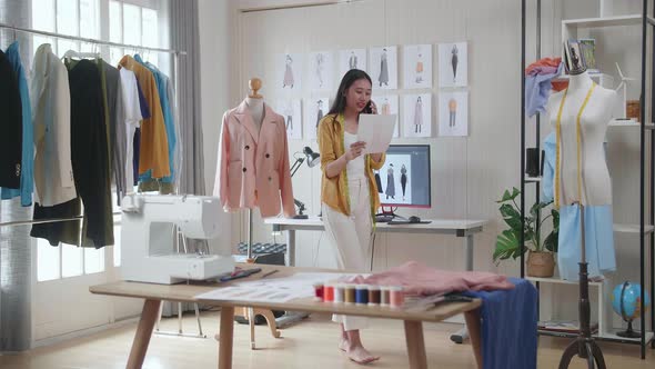 Female Designer With Sewing Machine Talking On Smartphone, Looking At Picture In Hand And Walking