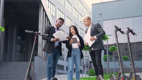 Young Mixed Race People Standing Near Modern Building and Revisioning Financial Documents