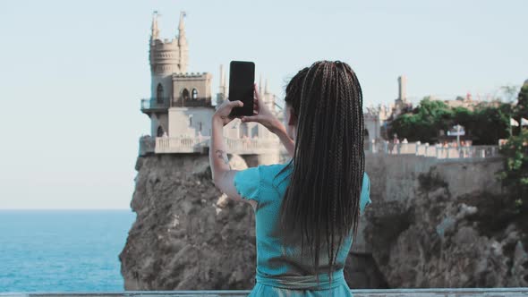 A Young Woman with Dreadlocks Stands on a Background of Sea and a Castle on the Edge Cliff Taking a